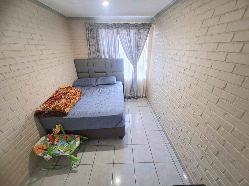 A compact bedroom featuring painted brick walls, ceramic floor tiling, and recessed ceiling lighting, providing a functional and neutral living space.