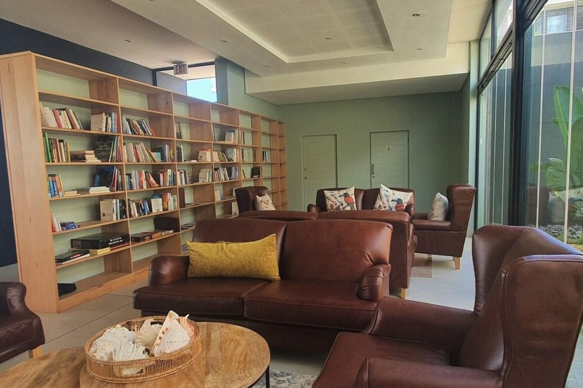 A spacious communal lounge area featuring extensive built-in wooden shelving, recessed lighting, and large glass doors providing natural light and garden views.