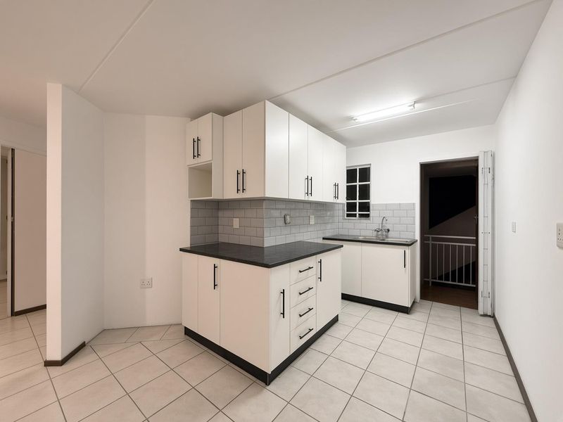 A clean, modern kitchen featuring white cabinetry, dark countertops, subway tile backsplash, and neutral ceramic floor tiles in an open, well-lit space.