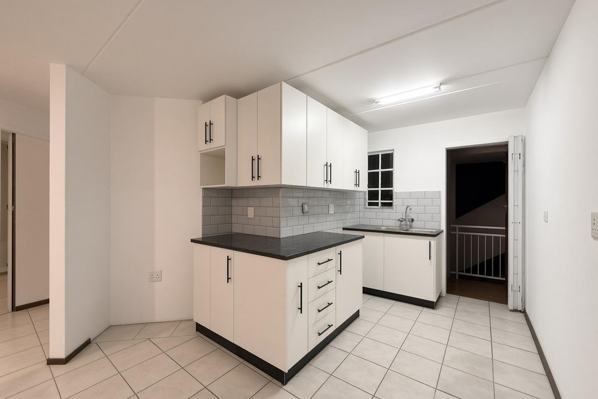 A clean, modern kitchen featuring white cabinetry, dark countertops, subway tile backsplash, and neutral ceramic floor tiles in an open, well-lit space.