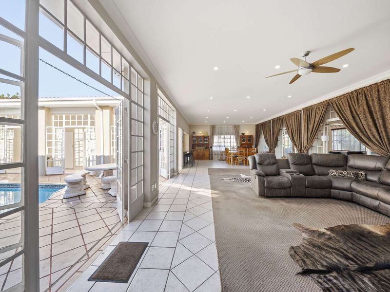 Spacious open-plan living area featuring tiled and carpeted floors, recessed lighting, and large french doors opening directly onto a private swimming pool area.