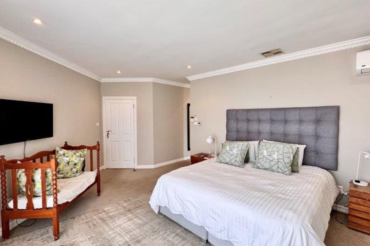 Spacious bedroom featuring neutral wall tones, crown molding, recessed lighting, and a wall-mounted split-system air conditioning unit.