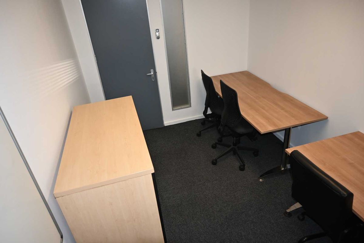 A functional office space featuring carpeted flooring, a solid core door, and a vertical sidelight window, providing a clean and professional work environment.