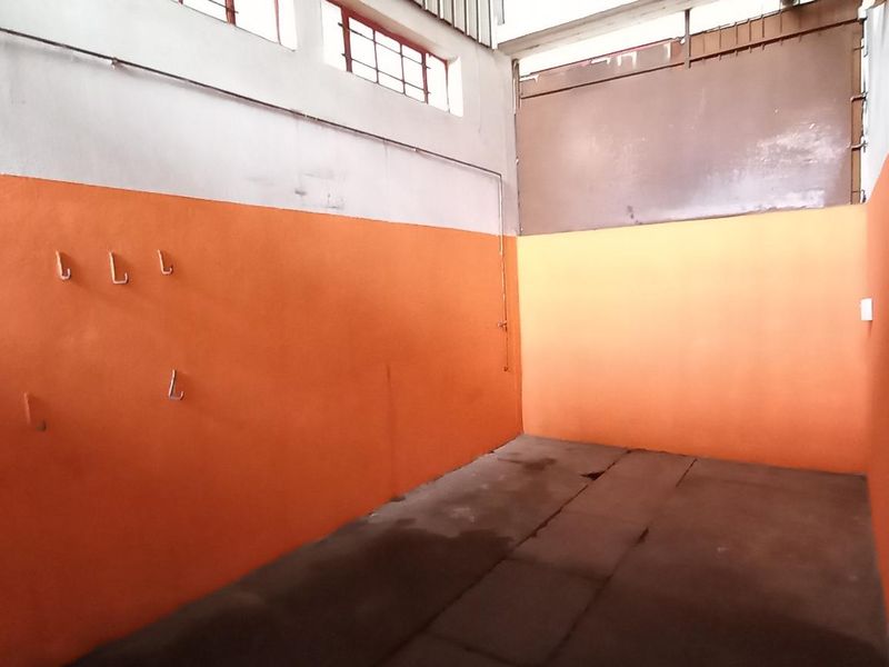 An empty industrial utility space featuring high-level windows, exposed electrical conduit, and wall-mounted storage hooks, suitable for workshop or storage use.