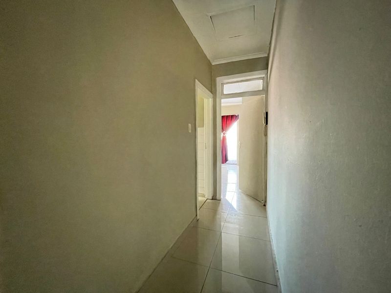 A simple, neutral-toned hallway featuring tiled flooring and a ceiling access hatch, providing a clean transition between living spaces.