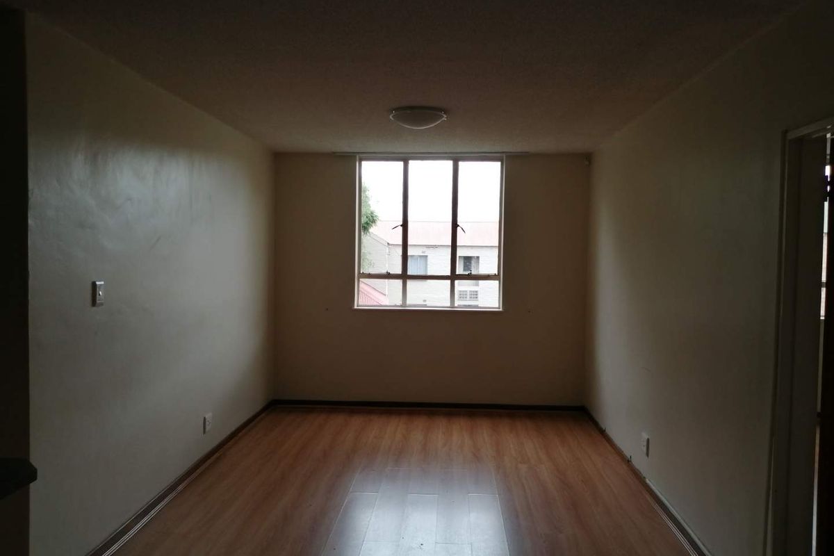 An empty living room featuring laminate flooring and a large window, providing a blank canvas for interior design and personalization.