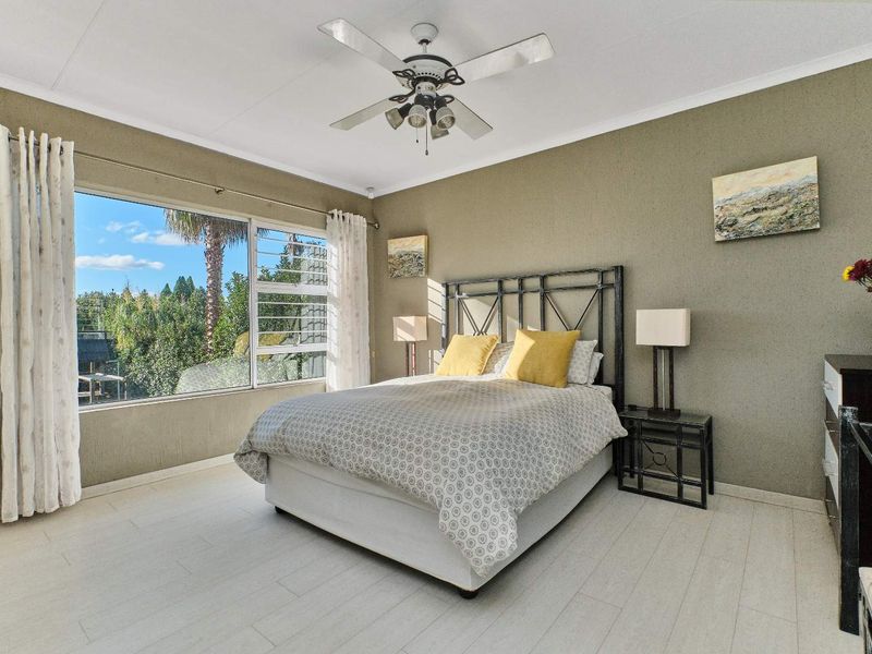 A well-lit bedroom featuring light-toned laminate flooring, a ceiling fan, and a large window providing natural light and garden views.