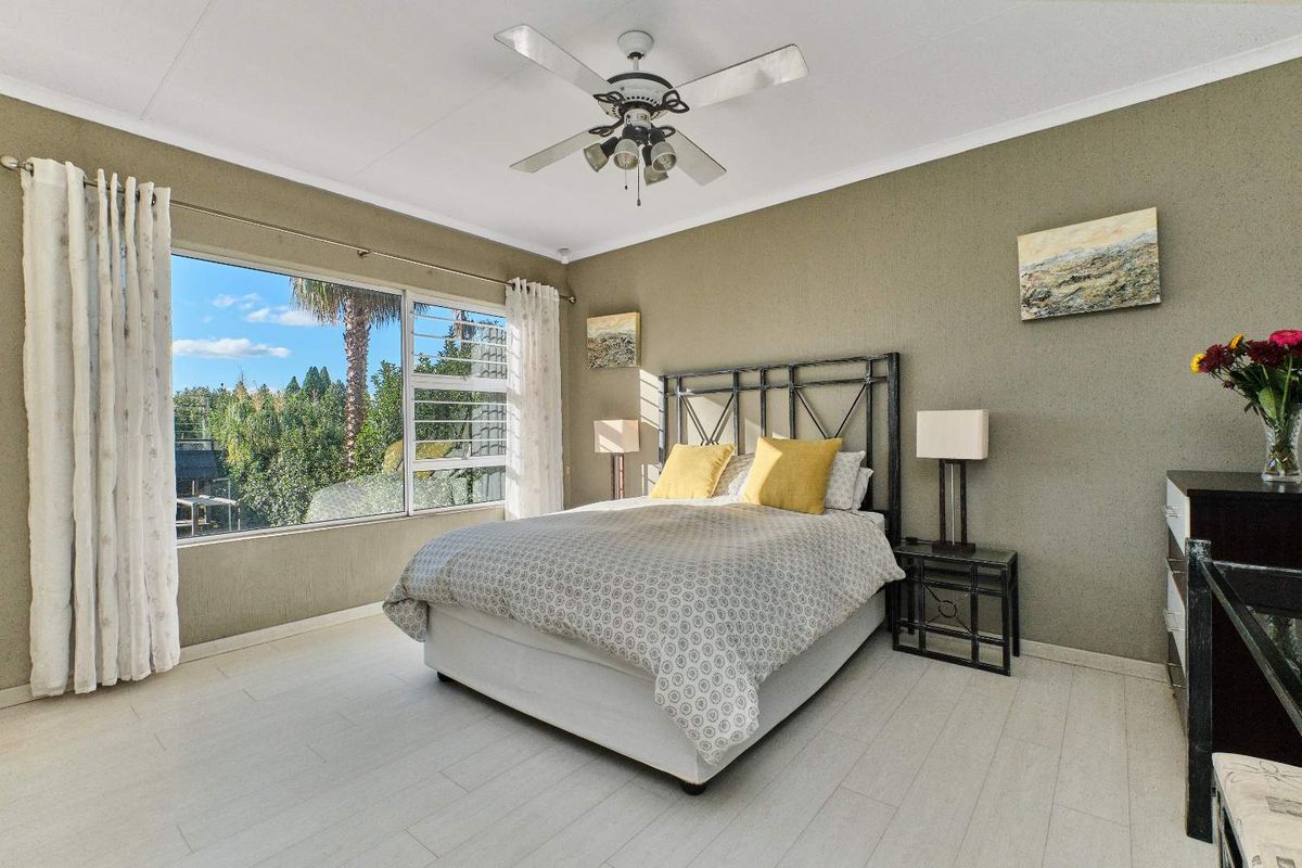 A well-lit bedroom featuring light-toned laminate flooring, a ceiling fan, and a large window providing natural light and garden views.