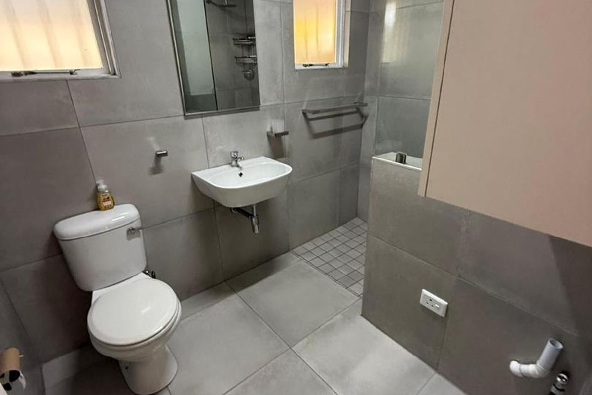 Modern bathroom featuring large format grey tiling, a wall-mounted basin, a toilet, and a walk-in shower area.