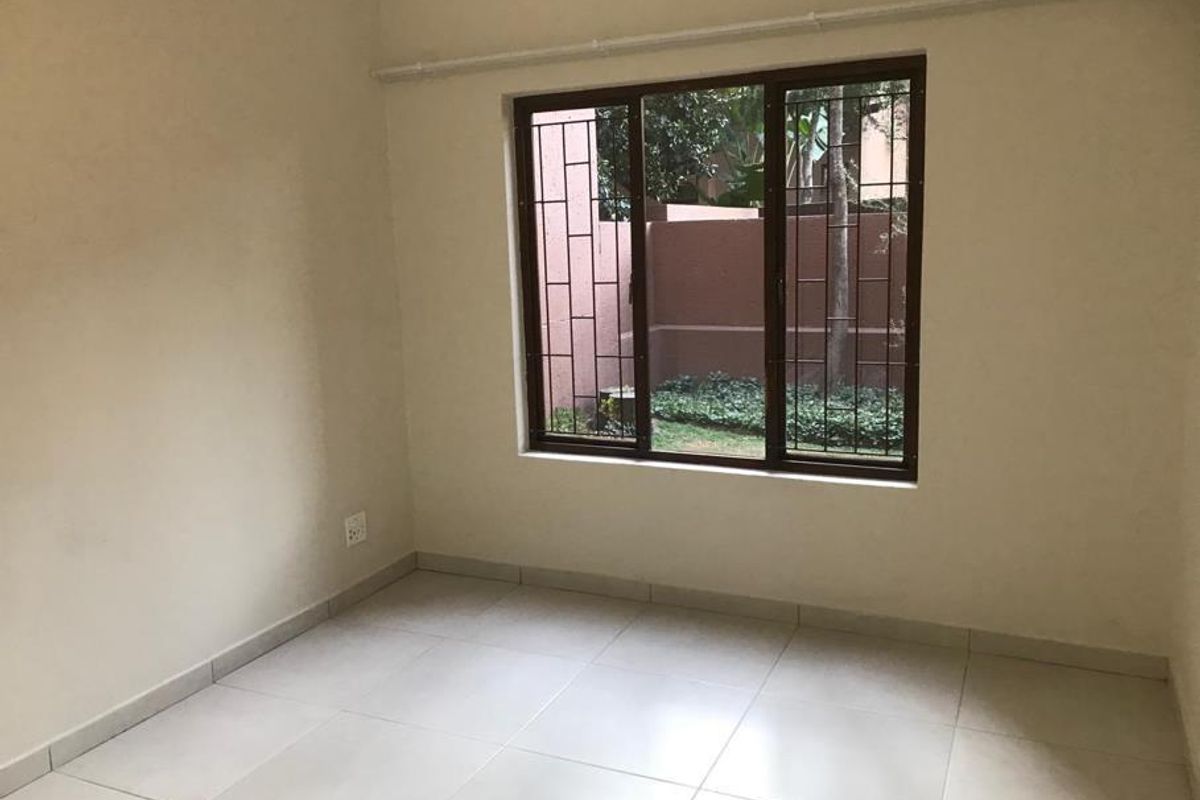 An empty bedroom featuring tiled flooring and a window with security bars, offering a neutral space ready for personalization.