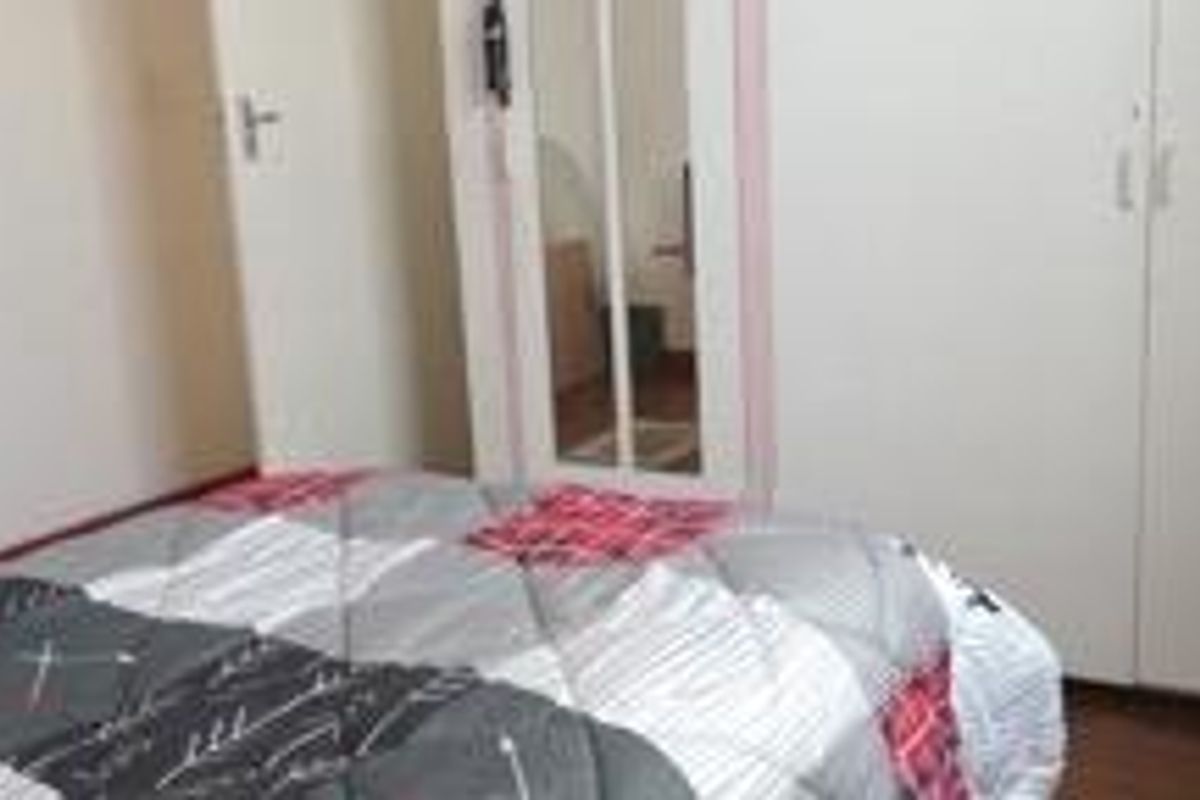 A bedroom featuring built-in cupboards with a central mirror panel and wooden flooring.