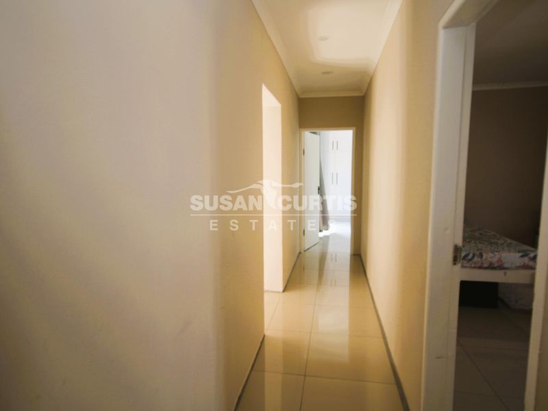 A clean, neutral-toned hallway featuring tiled flooring and recessed ceiling lighting, providing access to adjacent rooms.