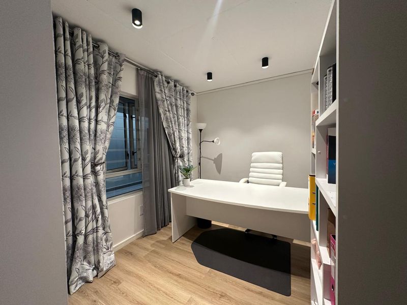 A well-lit home office featuring modern recessed ceiling spotlights, durable laminate flooring, and a practical built-in shelving unit for organized storage.