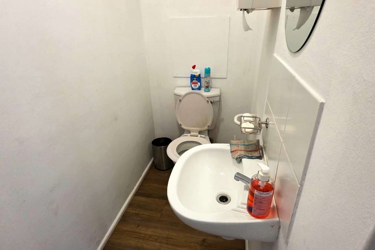 A compact office restroom featuring a wall-mounted basin and a standard toilet suite with wood-look flooring.