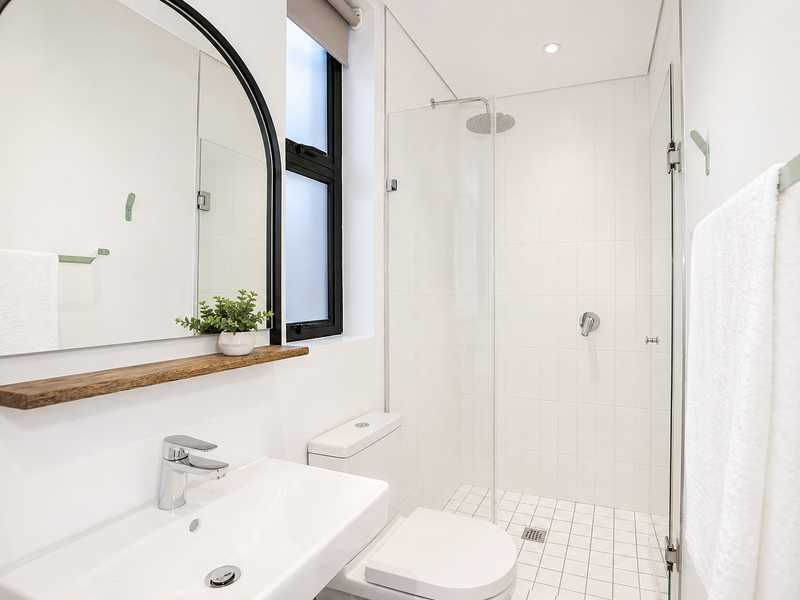 Modern bathroom featuring a walk-in shower with glass screen, white tiled finishes, contemporary basin with chrome mixer, and a sleek timber shelf.
