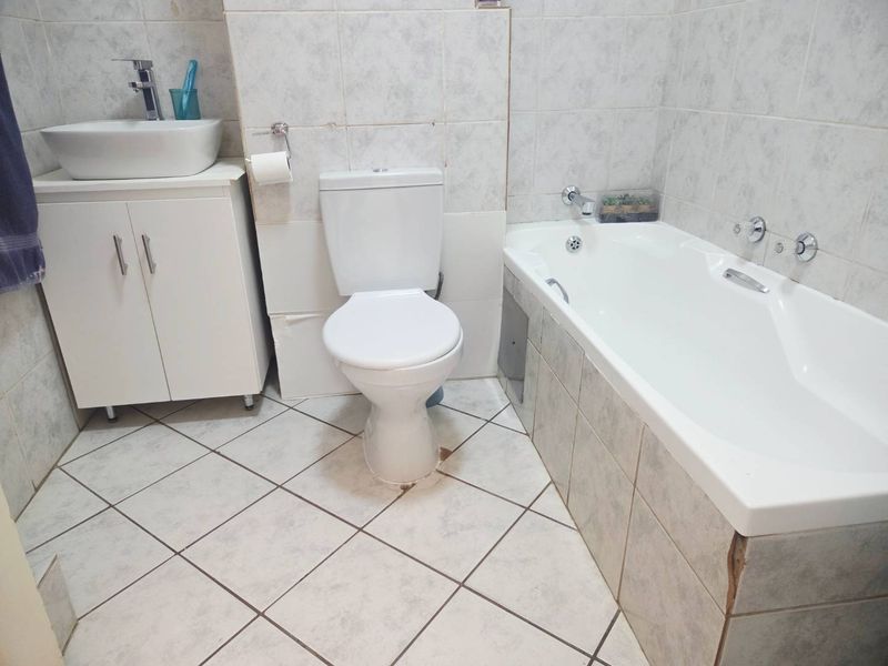 A functional bathroom featuring a vessel sink vanity, standard toilet, and a bathtub with tiled surround and flooring.