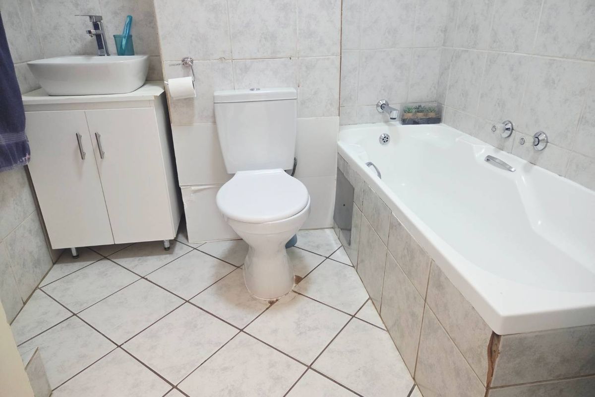A functional bathroom featuring a vessel sink vanity, standard toilet, and a bathtub with tiled surround and flooring.