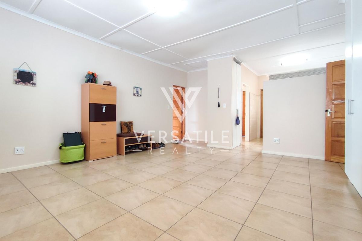 A spacious, open-plan living area featuring neutral tiled flooring, a grid-patterned ceiling, and multiple wooden interior doors.