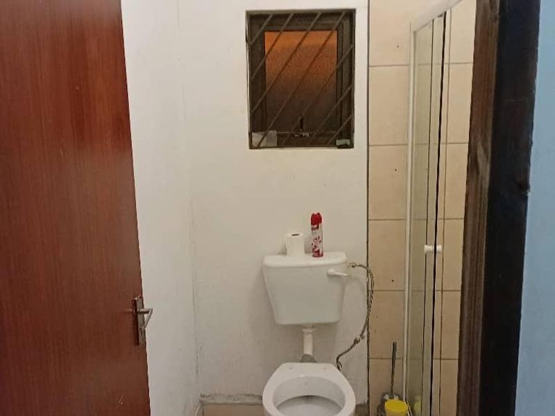 A compact bathroom featuring a toilet, shower enclosure with glass door, and tiled finishes. The space requires cosmetic updates and maintenance.