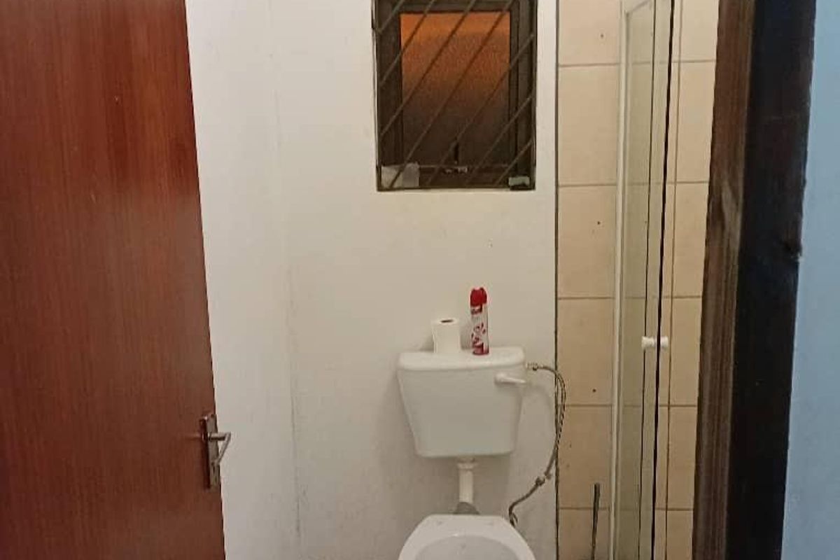 A compact bathroom featuring a toilet, shower enclosure with glass door, and tiled finishes. The space requires cosmetic updates and maintenance.