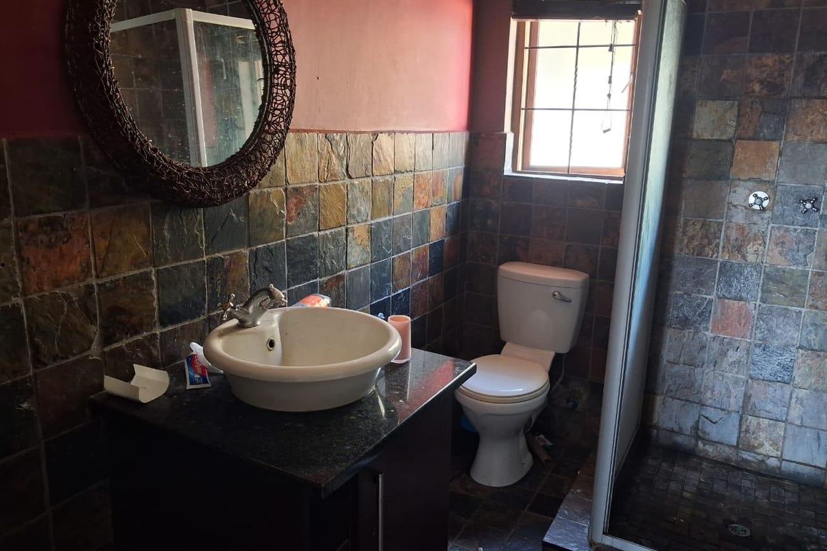 Bathroom featuring slate wall and floor tiling, a granite-topped vanity with vessel sink, toilet, and a glass-enclosed shower.