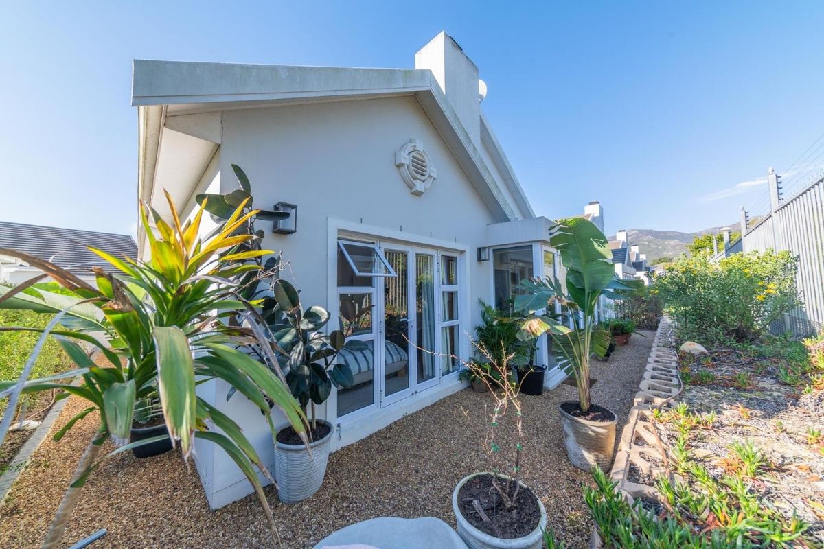 Rear exterior view of the property featuring a paved garden area, white framed glass doors, and a well-maintained building facade.