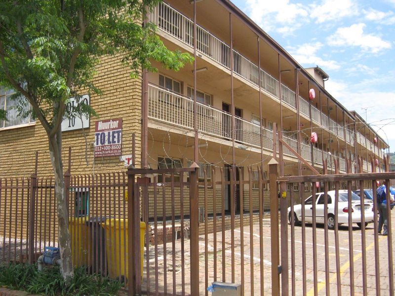 Exterior view of a multi-story apartment building featuring brick facade, metal security fencing, and balcony access for upper levels.