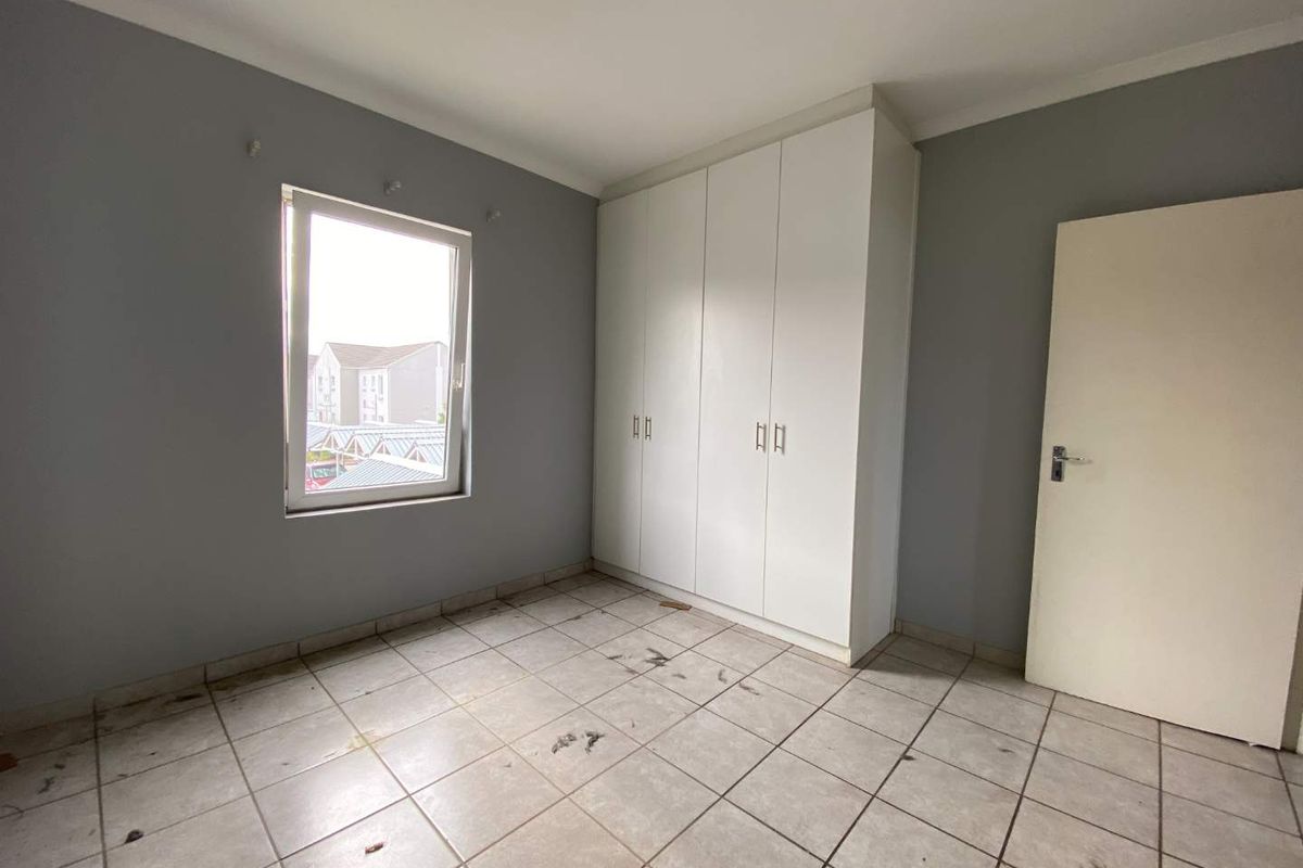 A vacant bedroom featuring built-in white cupboards, tiled flooring, and a window with a view of the surrounding apartment complex.