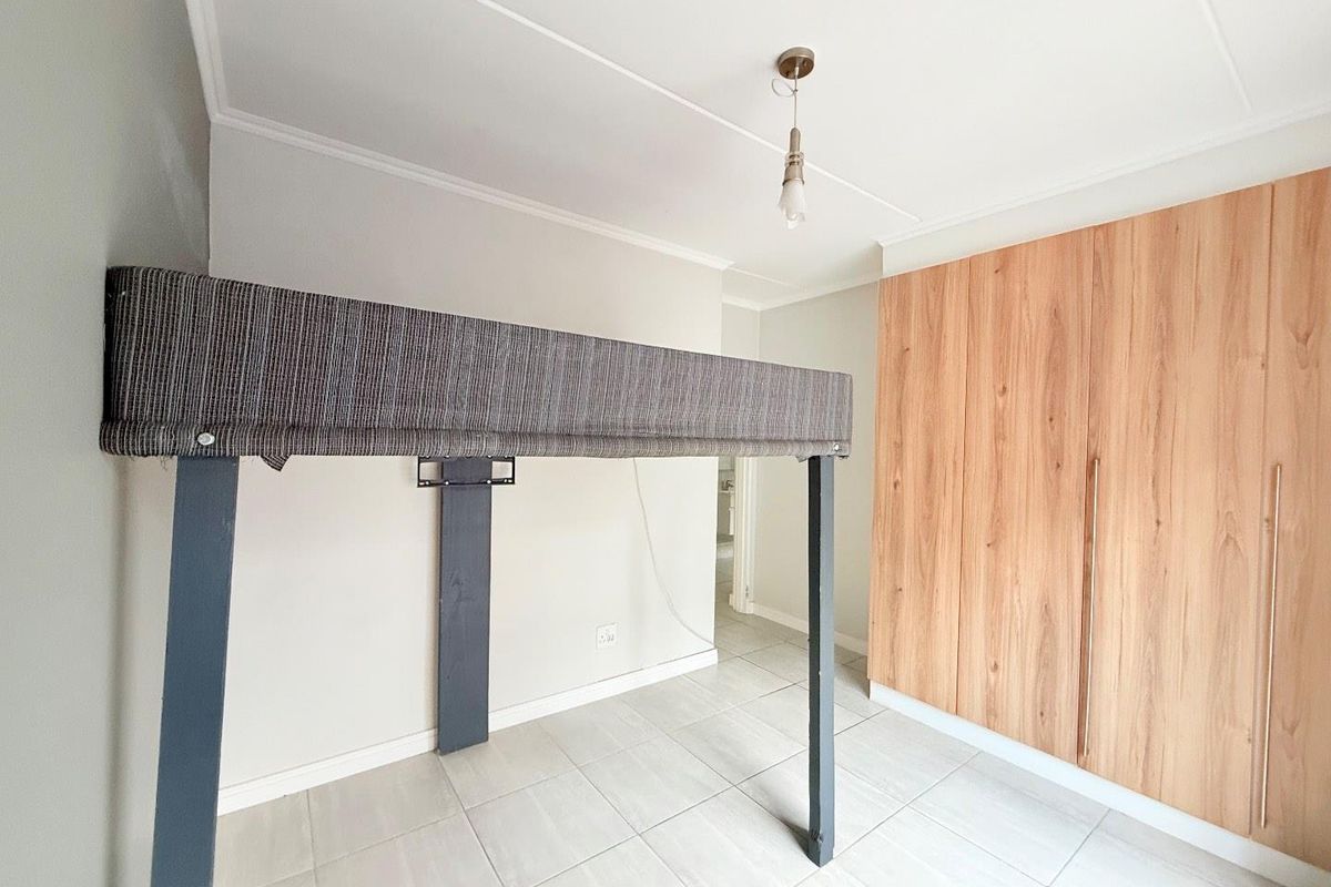 A bedroom featuring light-toned floor tiles, a built-in wooden wardrobe, and a neutral color palette, offering a clean and functional living space.