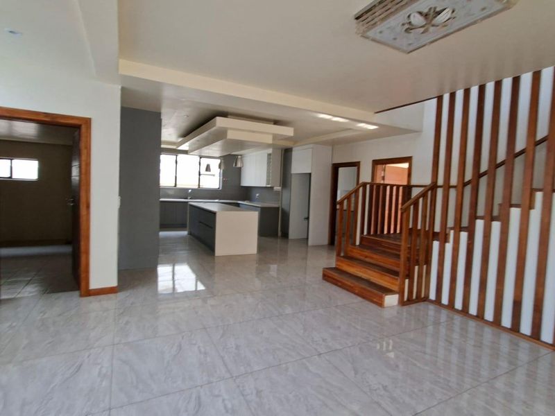 Spacious open-plan living area featuring a modern kitchen with a central island, tiled flooring, and a prominent wooden staircase with a matching balustrade.