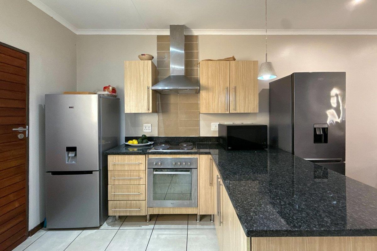 A functional kitchen featuring light wood cabinetry, dark granite countertops, a built-in oven, stainless steel extractor fan, and tiled flooring.