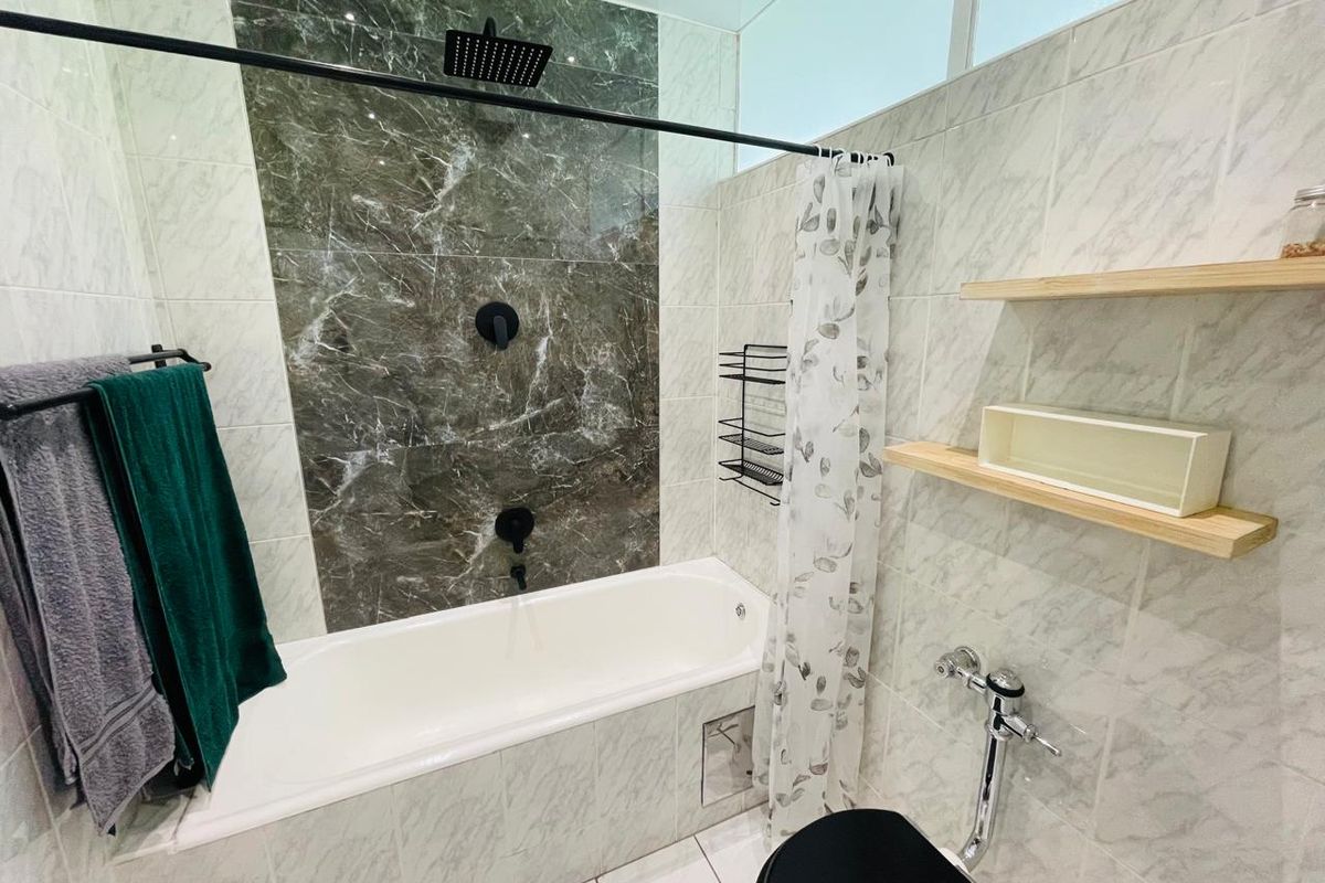 Modern bathroom featuring a bathtub with a dark marble-look feature wall, black rainfall showerhead, and contemporary fixtures.