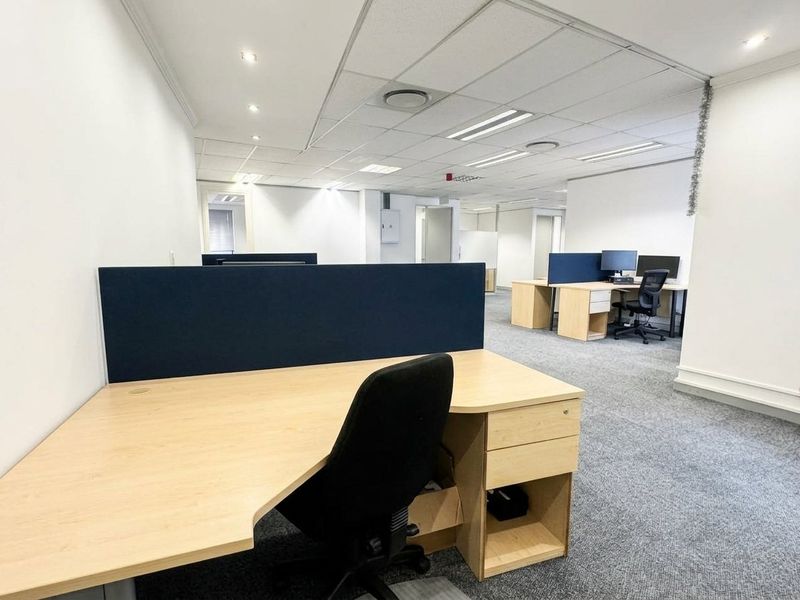 Open-plan office space featuring neutral carpeting, suspended ceiling with recessed lighting, and built-in workstation partitions.