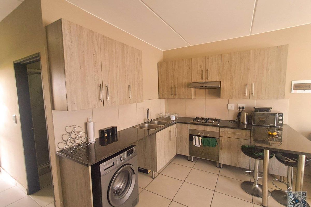 Modern kitchen featuring wood-look cabinetry, granite countertops, a built-in oven with gas hob, extractor fan, and integrated space for a washing machine.
