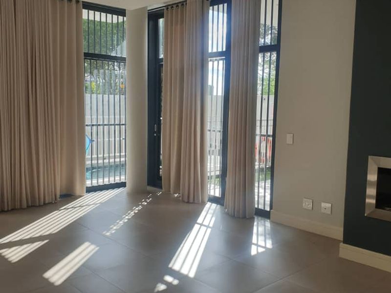 Spacious living area featuring large format floor tiles, a modern built-in fireplace, and floor-to-ceiling windows with direct access to the outdoor area.