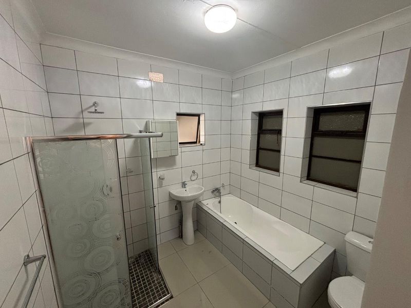 A functional bathroom featuring a separate shower enclosure, built-in bathtub, pedestal basin, and toilet with full-height wall tiling.