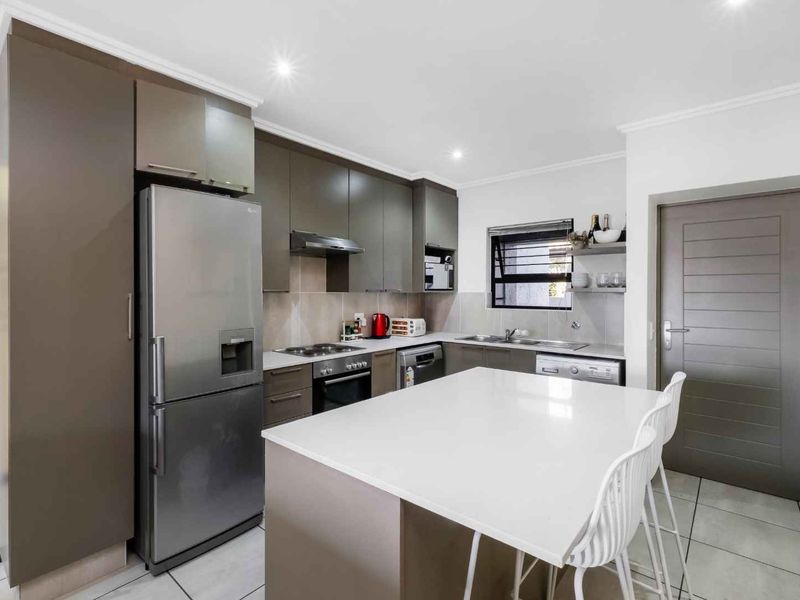 Modern kitchen featuring sleek cabinetry, stone countertops, a central island, and integrated appliances, finished with neutral tiled flooring and recessed lighting.
