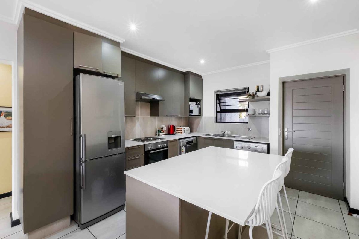 Modern kitchen featuring sleek cabinetry, stone countertops, a central island, and integrated appliances, finished with neutral tiled flooring and recessed lighting.