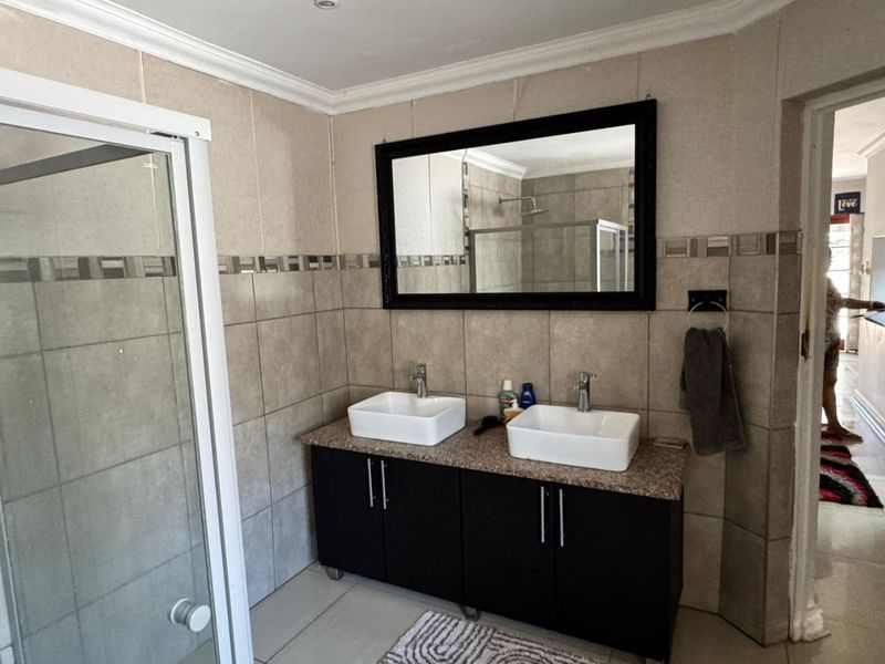 A well-maintained bathroom featuring a double vanity with vessel sinks, granite countertop, and a glass-enclosed shower with neutral wall and floor tiling.