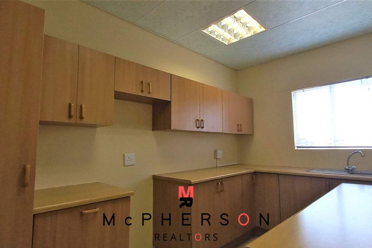 A functional kitchenette featuring wood-look cabinetry, laminate countertops, a stainless steel sink, and recessed ceiling lighting.