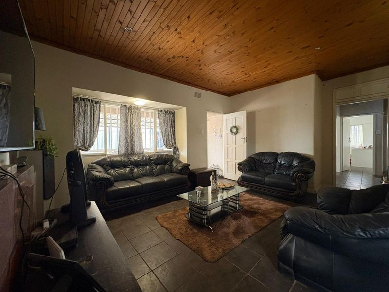 A living room featuring a timber tongue and groove ceiling, tiled flooring, and security bars on the windows.