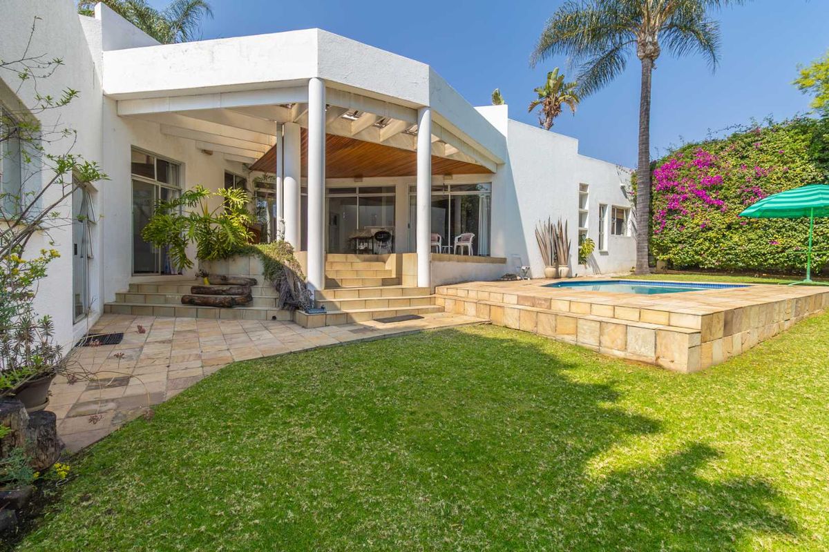 Rear view of the property featuring a covered patio, raised swimming pool, landscaped garden, and sliding glass doors providing access to the interior.