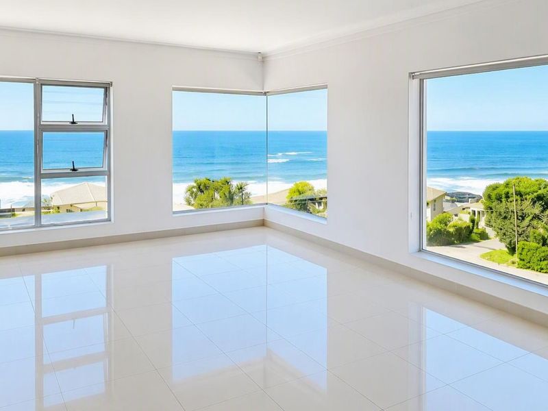 A bright, empty living area featuring large format floor tiles and expansive corner windows offering panoramic ocean views.
