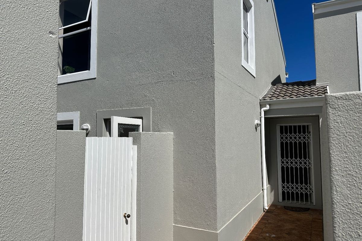 A side view of the property showing a paved walkway, security gate, and plastered exterior walls.