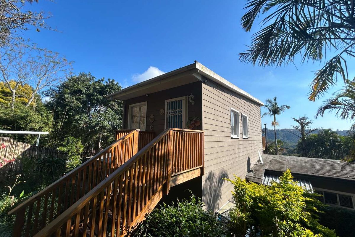 A charming elevated cottage featuring timber cladding, a wooden staircase with balustrade, and secure access, set within a lush, scenic garden environment.
