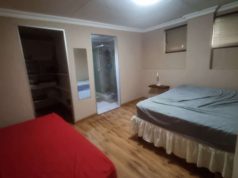 A bedroom featuring laminate flooring, cove cornicing, an en-suite bathroom, and a walk-in closet with built-in shelving.