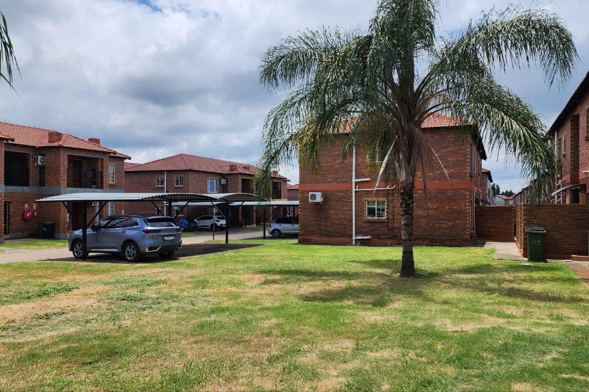Exterior view of a brick apartment complex featuring communal garden space and covered parking bays.