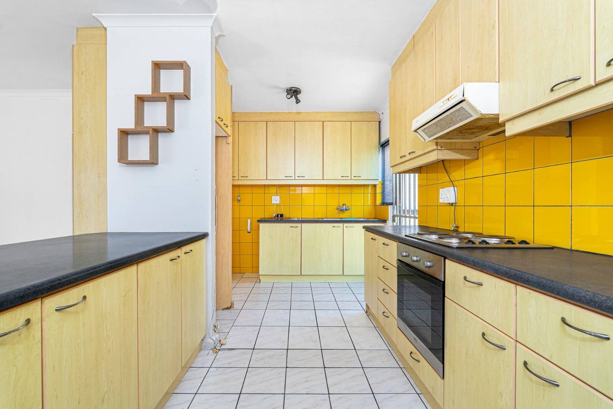 A functional kitchen featuring light wood-look cabinetry, a built-in oven with hob, extractor fan, and vibrant yellow tiled splashbacks.