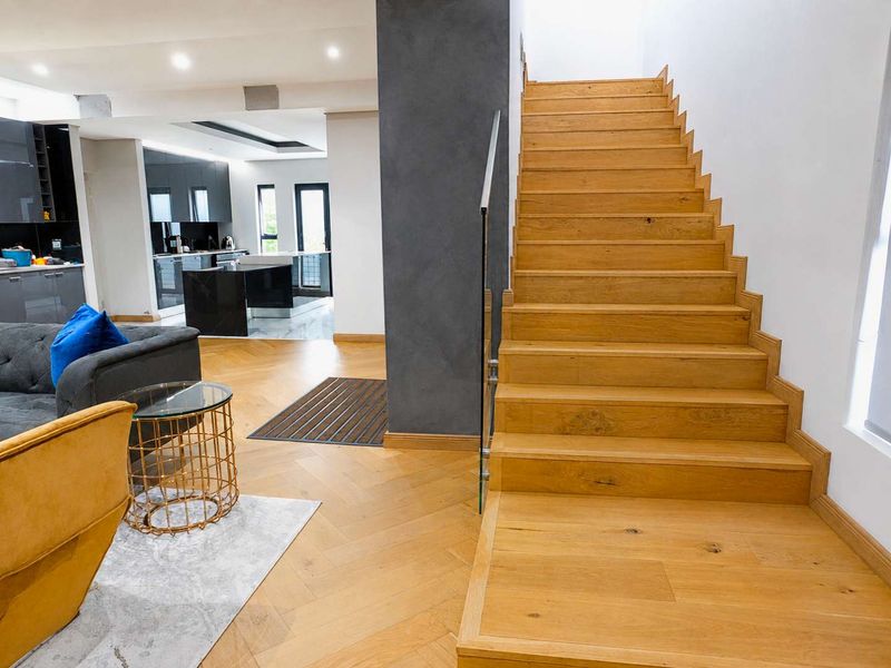 Modern open-plan living area featuring high-quality herringbone timber flooring, a striking timber staircase with glass balustrade, and a sleek contemporary kitchen.