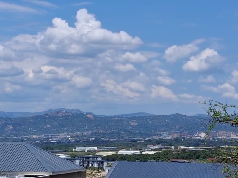 A scenic elevated view overlooking the surrounding landscape, distant hills, and urban development under a bright, cloudy sky.
